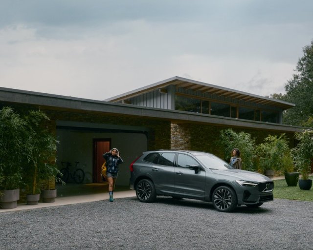 SUV hibrida Volvo XC60 color gris estacionada en el porche de una casa con una mujer caminando al lado.